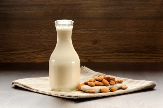 Almond milk in bottle with raw almonds on striped napkin