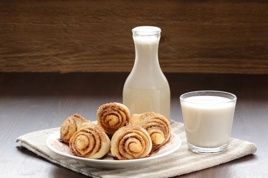 Cinnamon rolls with glass and bottle of milk on wood table