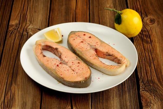 Salmon steakes with lemon on white plate on wood table