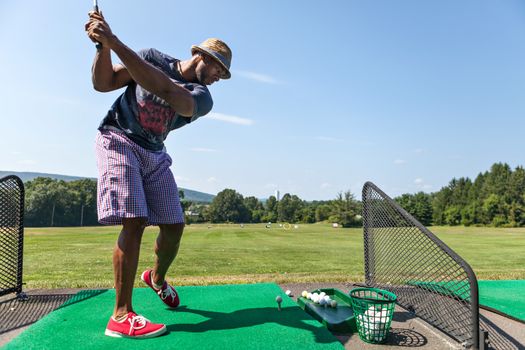 Athletic golfer swinging at the driving range dressed in casual attire.