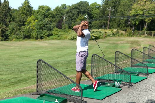 Athletic golfer swinging at the driving range dressed in casual attire.