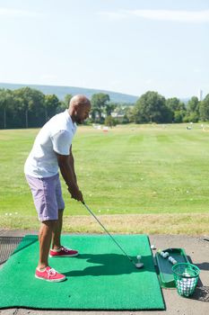 Athletic golfer teeing off at the driving range dressed in casual attire.