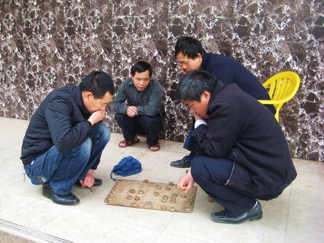 A group of man is playing Chinese chess on the floor.