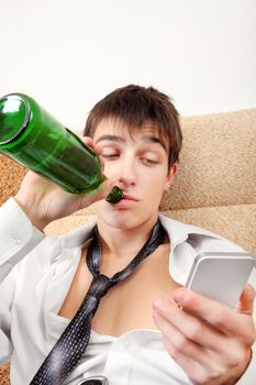 Young Man with Bottle of the Beer and Cellphone on the Sofa at the Home