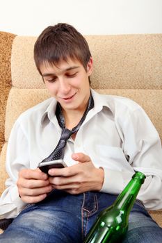 Young Man with Bottle of the Beer and Cellphone on the Sofa at the Home