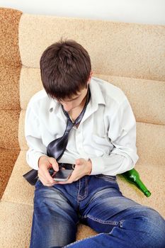 Teenager with Bottle of the Beer and Cellphone on the Sofa at the Home