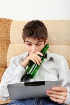 Stressed and Tired Teenager with a Beer and Tablet Computer on the Sofa at the Home