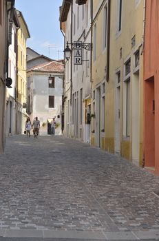 Some people walking by a narrow street in the historical part of the town of Bassano del Grappa, Northern Italy