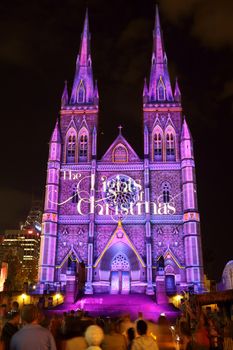 SYDNEY, AUSTRALIA - DECEMBER 23, 2014; Crowds of people on the forecourt of St Mary's Cathedral Sydney CBD watch and enjoy the Christmas lights display.  One of the many visions projected on the church building sandstone facade at Christmas time.