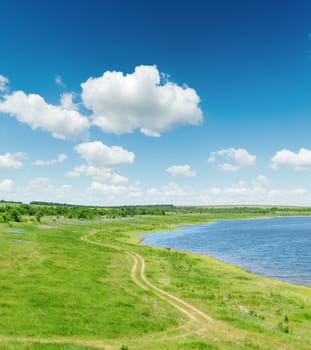 green landscape with road and pond under blue sky with white clouds