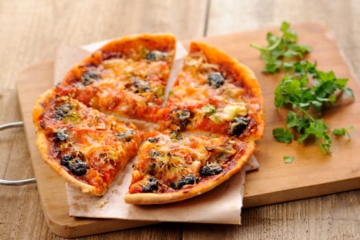 Pizza with olives and salmon and fresh greens on wooden board