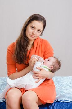 Six month old baby drinking milk from a bottle with a nipple, lying on his mother's arms