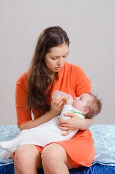 Six month old baby drinking milk from a bottle with a nipple, lying on his mother's arms