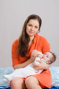 Six month old baby drinking milk from a bottle with a nipple, lying on his mother's arms