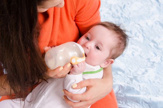 Six month old baby drinking milk from a bottle with a nipple, lying on his mother's arms
