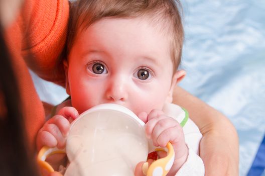 Six month old baby drinking milk from a bottle with a nipple, lying on his mother's arms