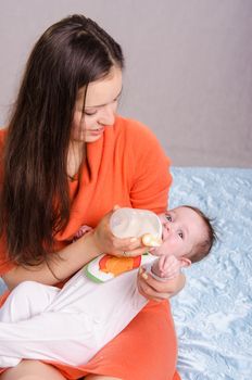 Six month old baby drinking milk from a bottle with a nipple, lying on his mother's arms