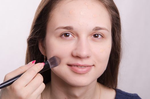 Makeup artist applies foundation of a beautiful young girl in the makeup