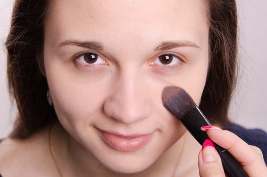 Makeup artist applies foundation of a beautiful young girl in the makeup