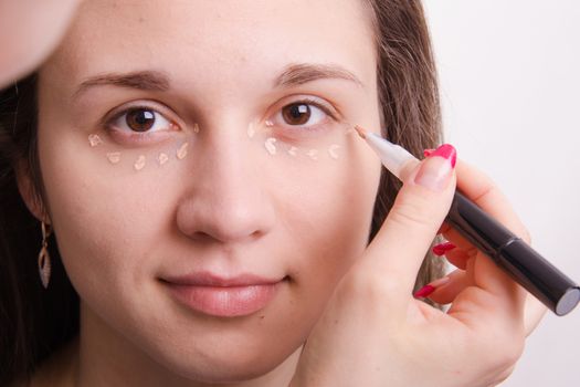 Makeup artist applies foundation of a beautiful young girl in the makeup
