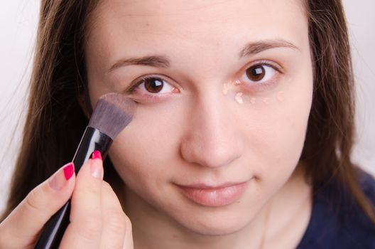 Makeup artist applies foundation of a beautiful young girl in the makeup