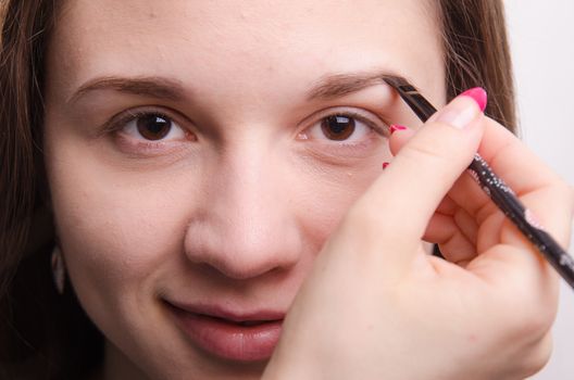 Makeup artist paints the eyebrows of a beautiful young girl in the makeup