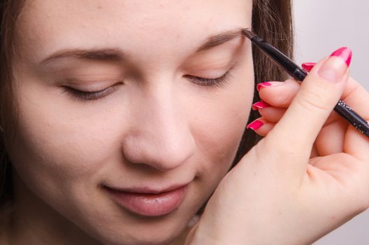 Makeup artist paints the eyebrows of a beautiful young girl in the makeup