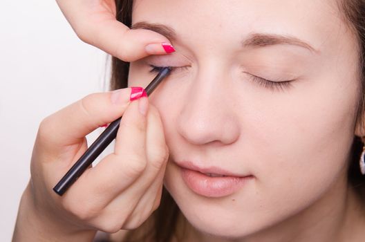 Makeup artist paints eyelashes of a beautiful young girl in the makeup