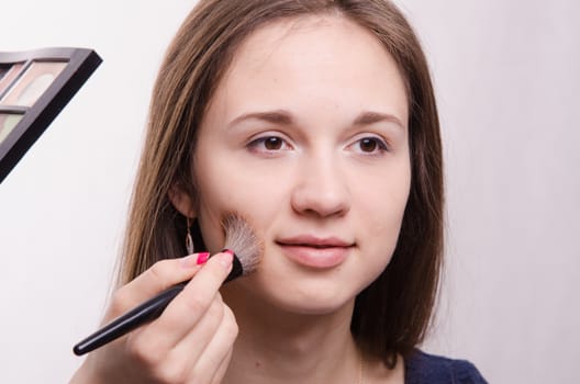 Makeup artist applies powder on the face of a beautiful young girl in the makeup