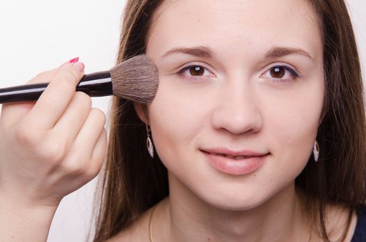 Makeup artist applies powder on the face of a beautiful young girl in the makeup