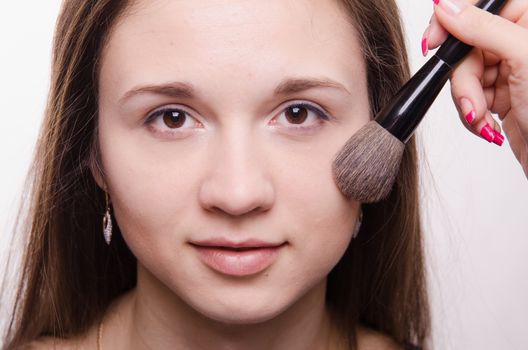 Makeup artist applies powder on the face of a beautiful young girl in the makeup
