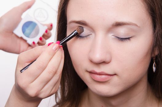 Makeup artist paints the eyelids of a beautiful young girl in the makeup