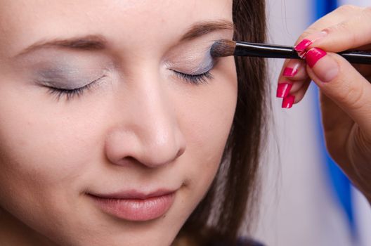 Makeup artist paints the eyelids of a beautiful young girl in the makeup