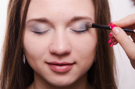 Makeup artist paints the eyelids of a beautiful young girl in the makeup