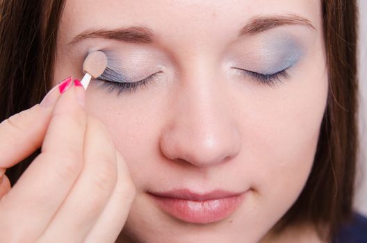 Makeup artist paints the eyelids of a beautiful young girl in the makeup