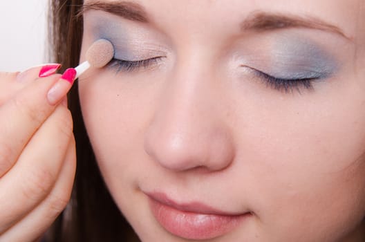 Makeup artist paints the eyelids of a beautiful young girl in the makeup