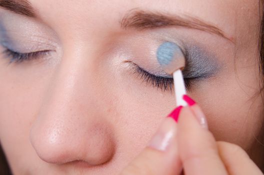 Makeup artist paints the eyelids of a beautiful young girl in the makeup