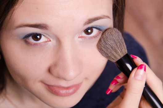 Makeup artist applies powder on the face of a beautiful young girl in the makeup