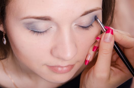 Makeup artist paints the eyelids of a beautiful young girl in the makeup