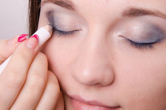 Makeup artist paints the eyelids of a beautiful young girl in the makeup