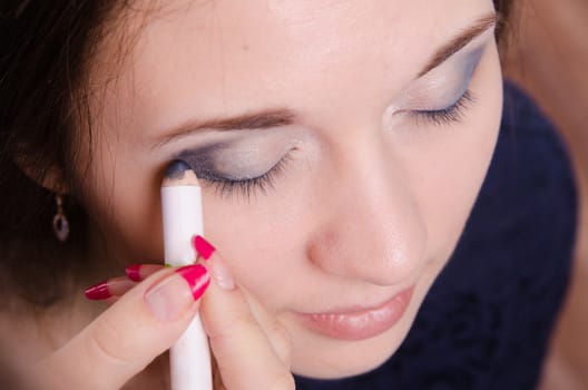 Makeup artist paints the eyelids of a beautiful young girl in the makeup