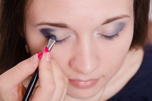 Makeup artist paints the eyelids of a beautiful young girl in the makeup