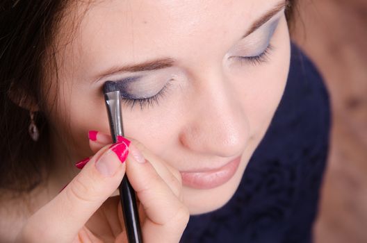 Makeup artist paints the eyelids of a beautiful young girl in the makeup