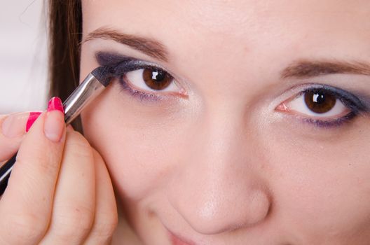 Makeup artist paints the eyelids of a beautiful young girl in the makeup