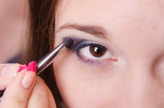 Makeup artist paints the eyelids of a beautiful young girl in the makeup