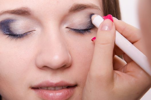 Makeup artist paints the eyelids of a beautiful young girl in the makeup
