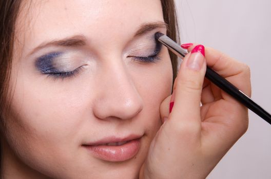 Makeup artist paints the eyelids of a beautiful young girl in the makeup