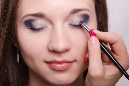 Makeup artist paints the eyelids of a beautiful young girl in the makeup