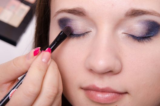 Makeup artist paints the eyelids of a beautiful young girl in the makeup