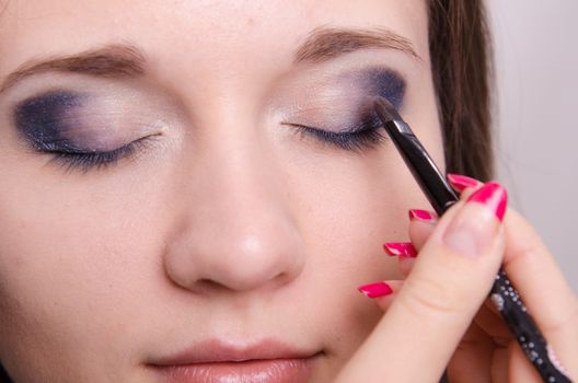 Makeup artist paints the eyelids of a beautiful young girl in the makeup